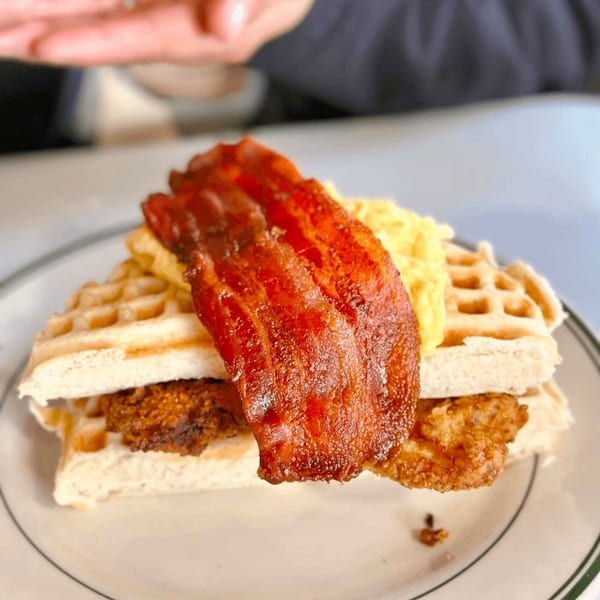 A diner-style waffle sandwich with crispy fried chicken, scrambled eggs, and bacon on a plate.