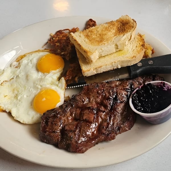 A diner breakfast with steak, two fried eggs, hash browns, toast, and a side of jam.