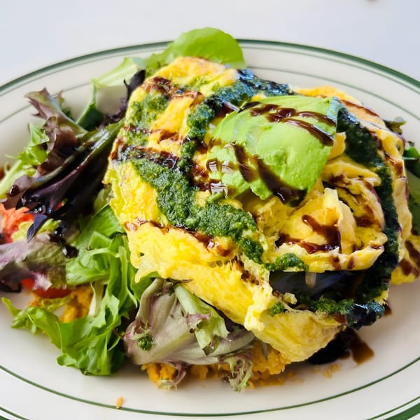 A Jax At The Tracks omelet with pesto, avocado, and balsamic glaze, served with a side salad.