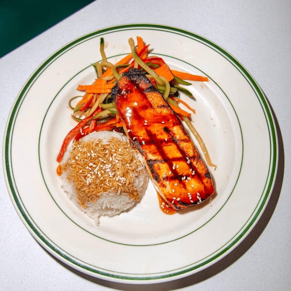 Grilled salmon with teriyaki glaze, white rice, and julienned vegetables on a diner plate.