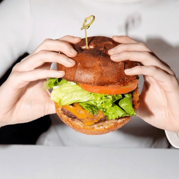 Hands holding a Jax At The Tracks burger with lettuce, tomato, and melted cheese.