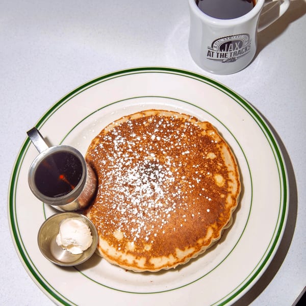 A Jax At The Tracks pancake with powdered sugar, syrup, butter, and coffee.