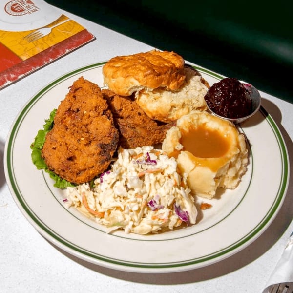 A diner plate with fried chicken, biscuits, mashed potatoes with gravy, coleslaw, and jam.
