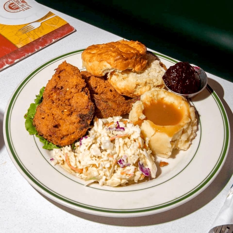A diner plate with fried chicken, biscuits, mashed potatoes with gravy, coleslaw, and jam.
